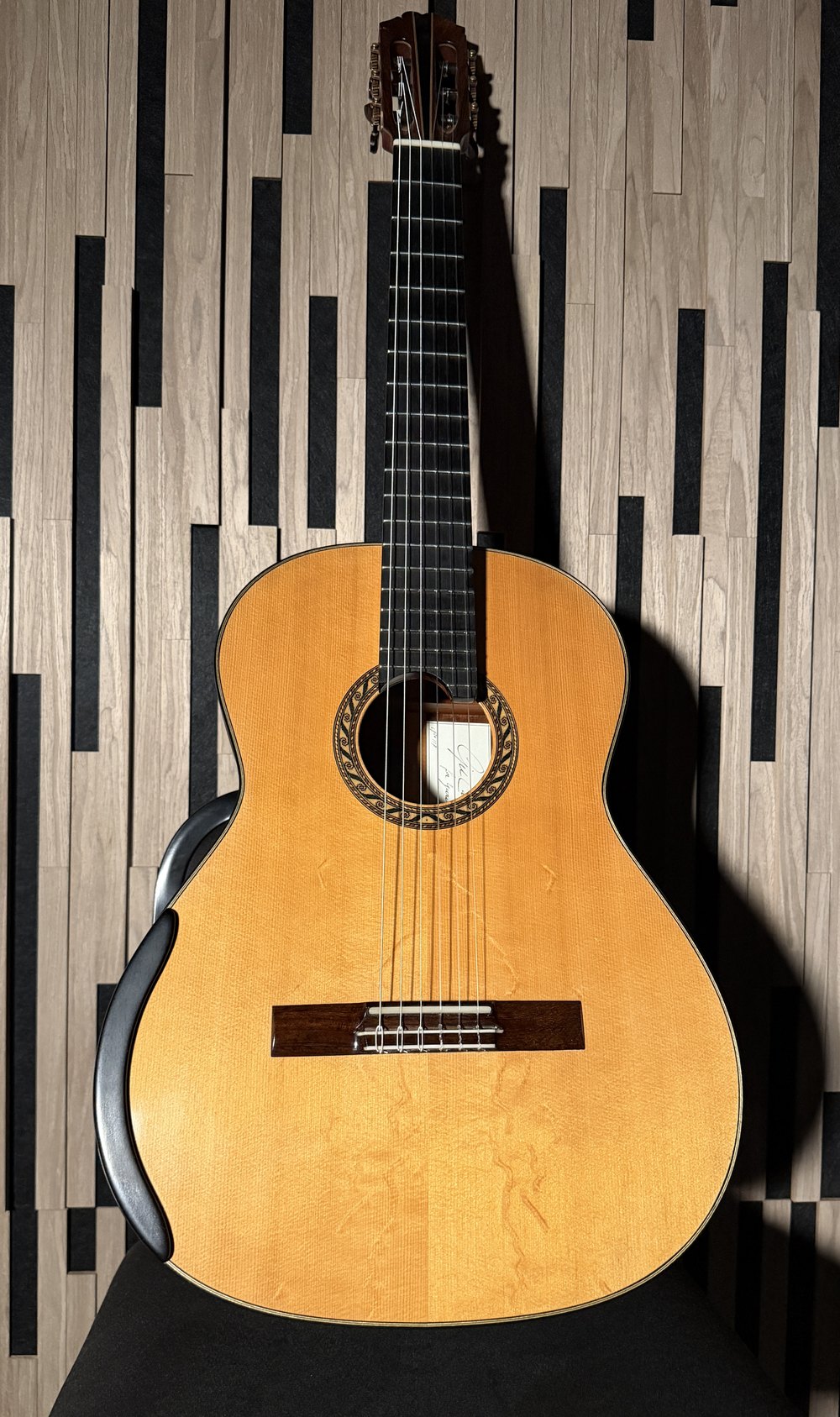 Gil Carnal № 117 standing against a wall: bear-claw German spruce top with rippled figure across the lower bout, blue scrolled rosette, a built-in armrest along the bass edge