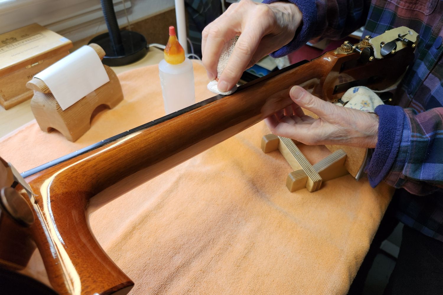 Cyndy Burton's hands touching up the finish on the neck of a classical guitar resting on a padded cradle