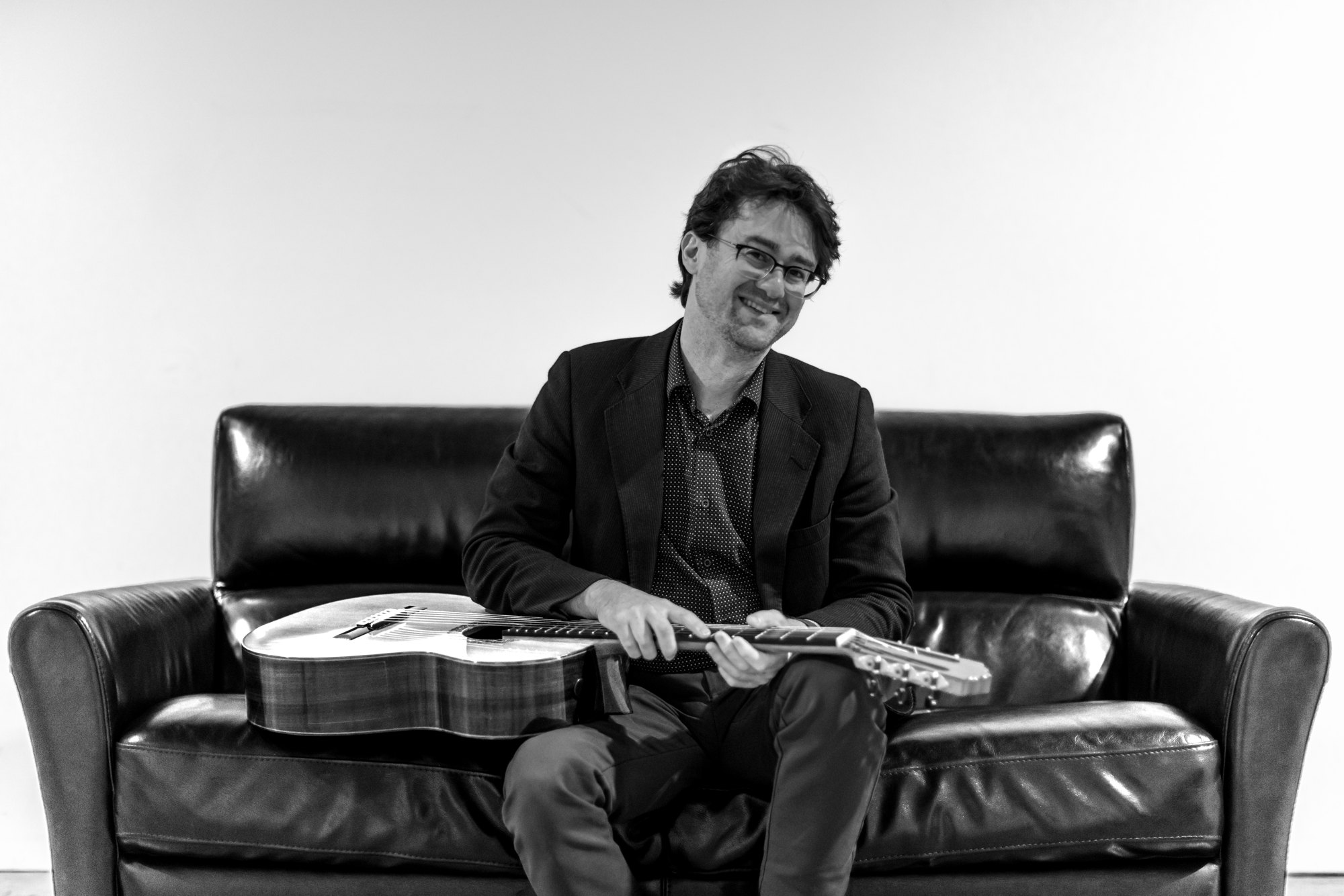 Yuri Liberzon laughing with his guitar on a leather couch