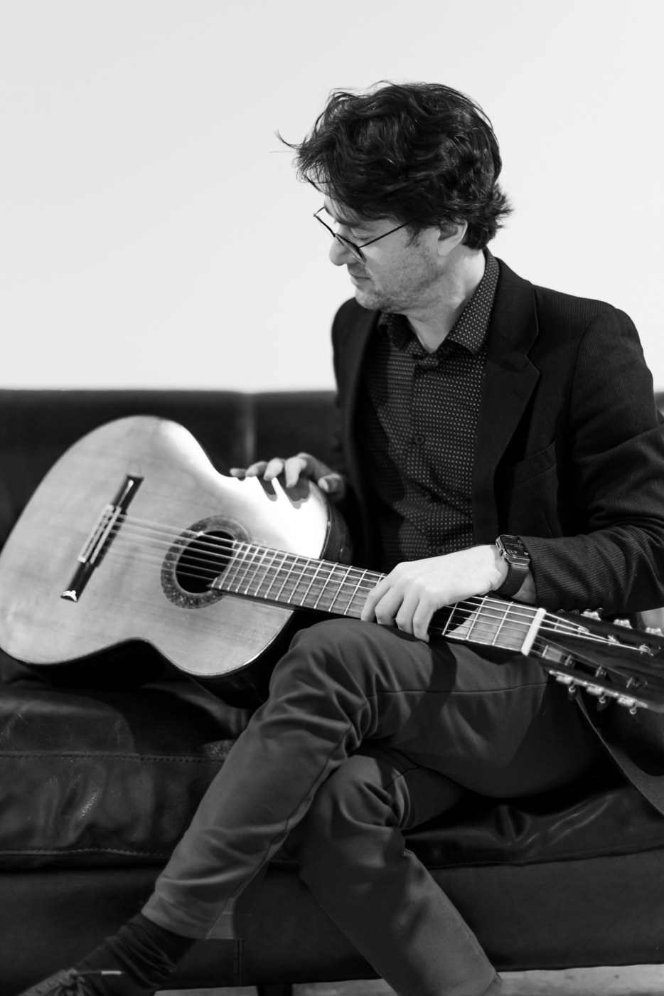 Yuri Liberzon seated on a couch, absorbed in his guitar