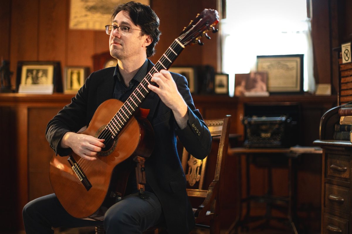 Yuri Liberzon listening, guitar in hand, in a wood-panelled room